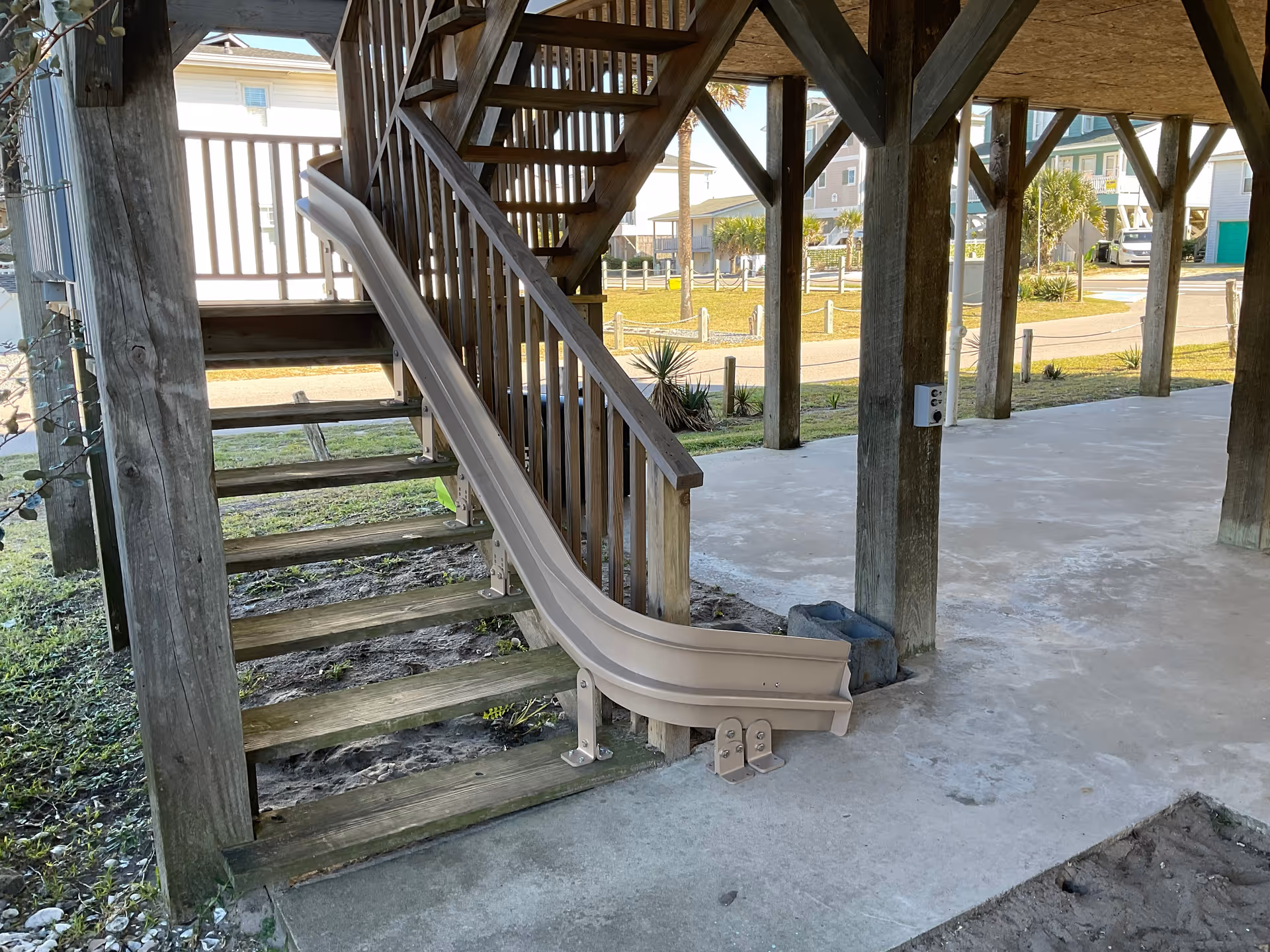 Outdoor wooden staircase with a beige slide under a covered structure.