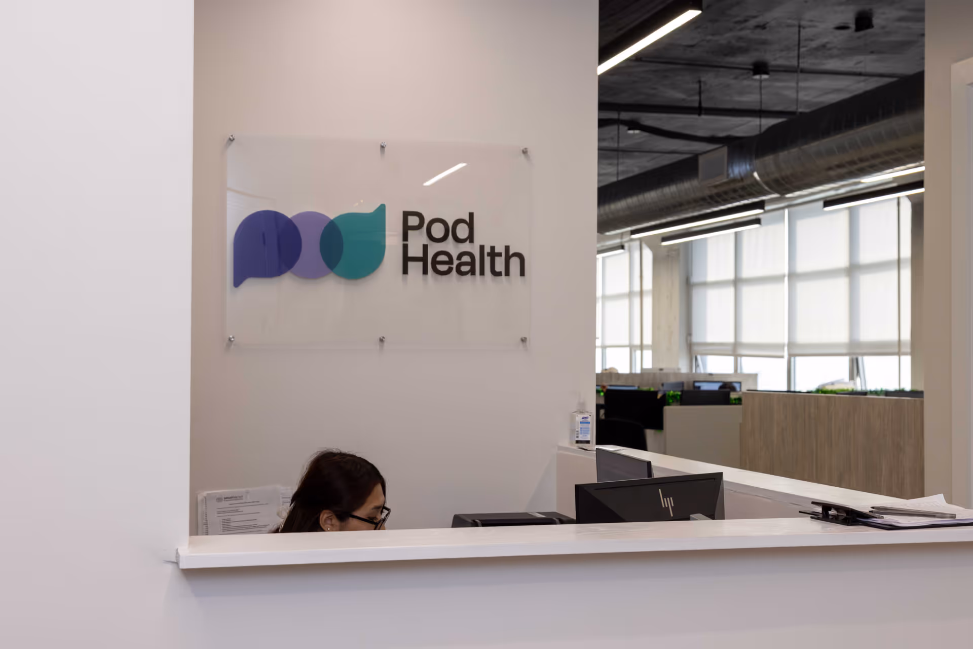 Reception desk with Pod Health sign and a person working at a computer inside an office.