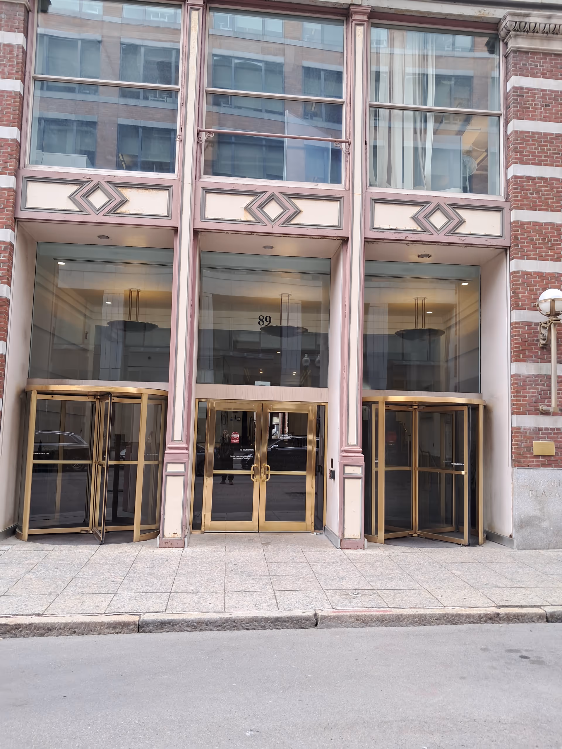 Facade of a brick building with large glass doors and gold-framed revolving entrances.