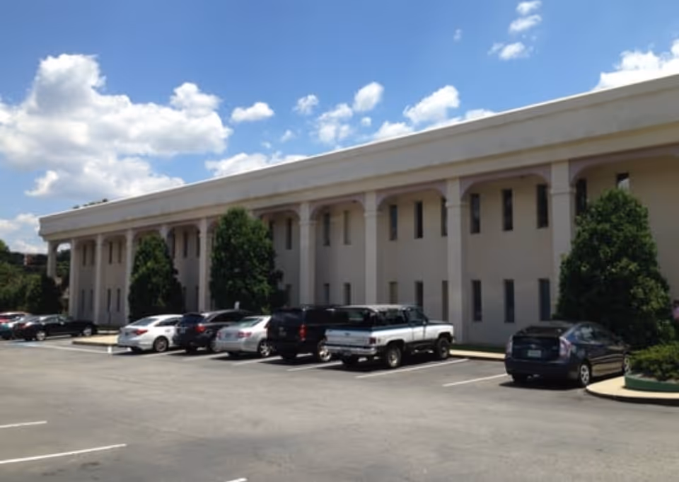 Exterior view of a long beige senior living facility with a parking lot and trees.