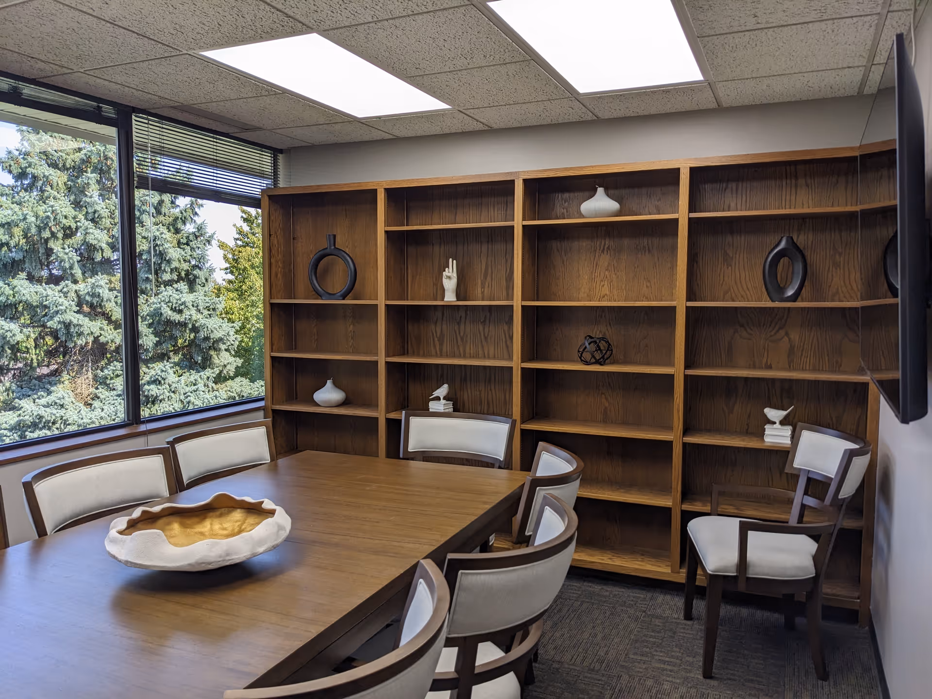 A meeting room with wooden bookshelves, a large table, and several chairs by a window.