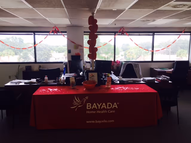 Indoor BAYADA Assistive Care event setup with a red branded table and office desks.