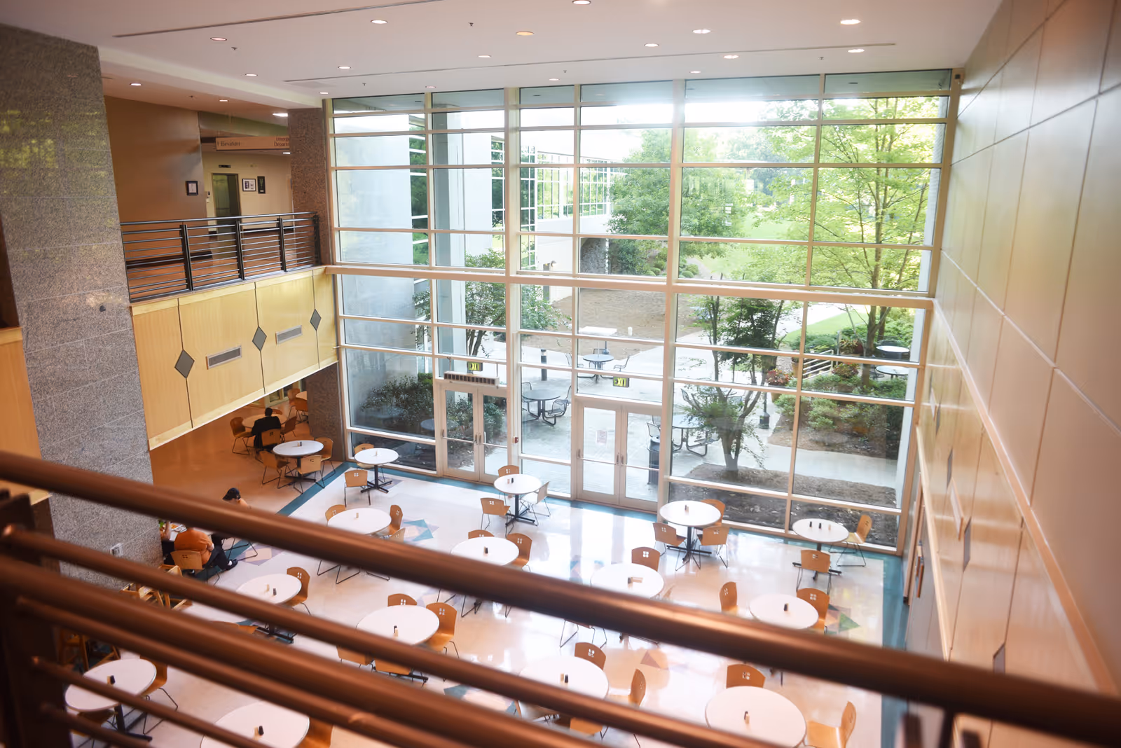 Bright interior atrium with large glass walls, round tables, and chairs overlooking a courtyard.