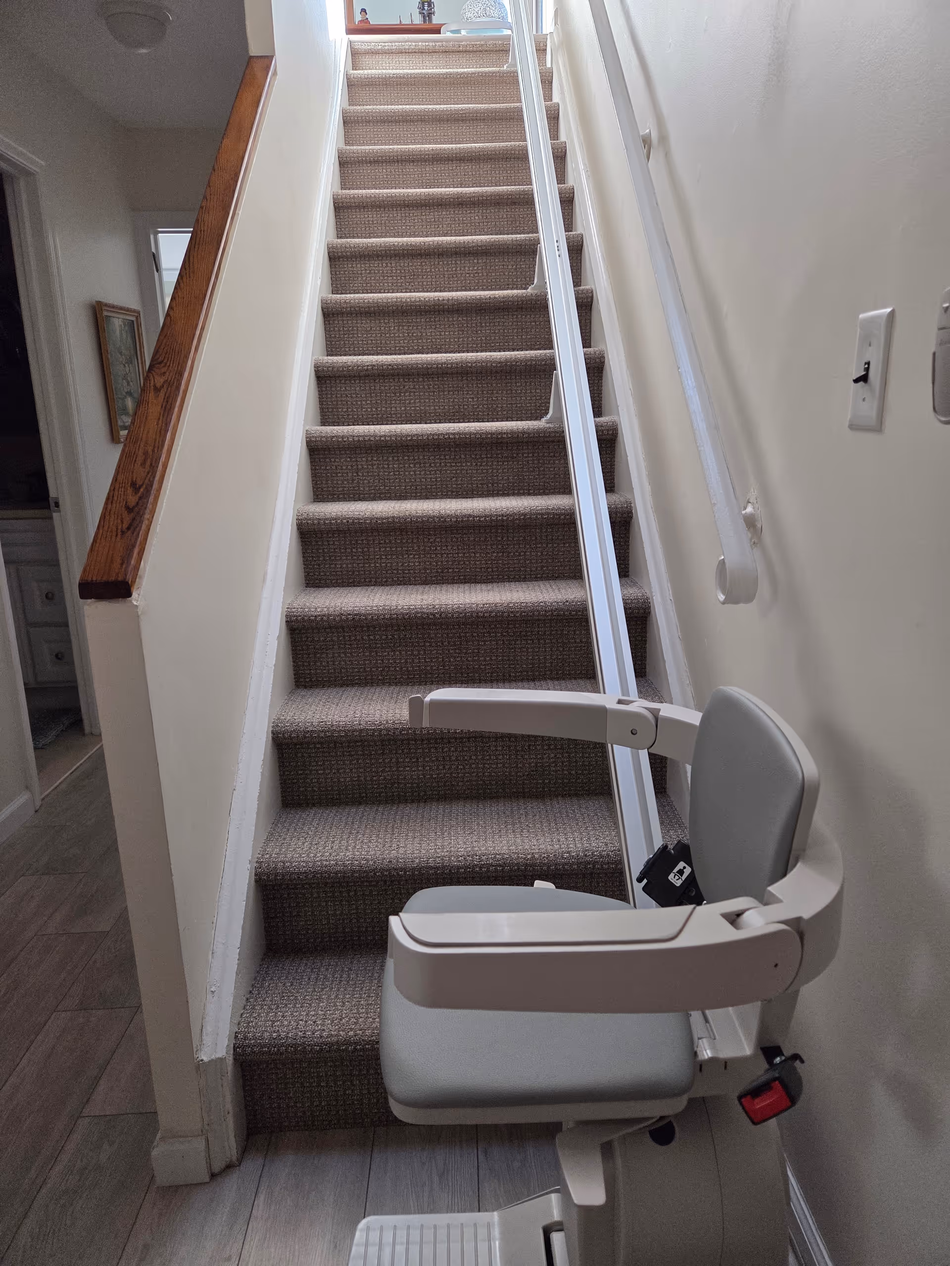 Indoor staircase with beige carpet and a wall-mounted stairlift chair in a senior living facility