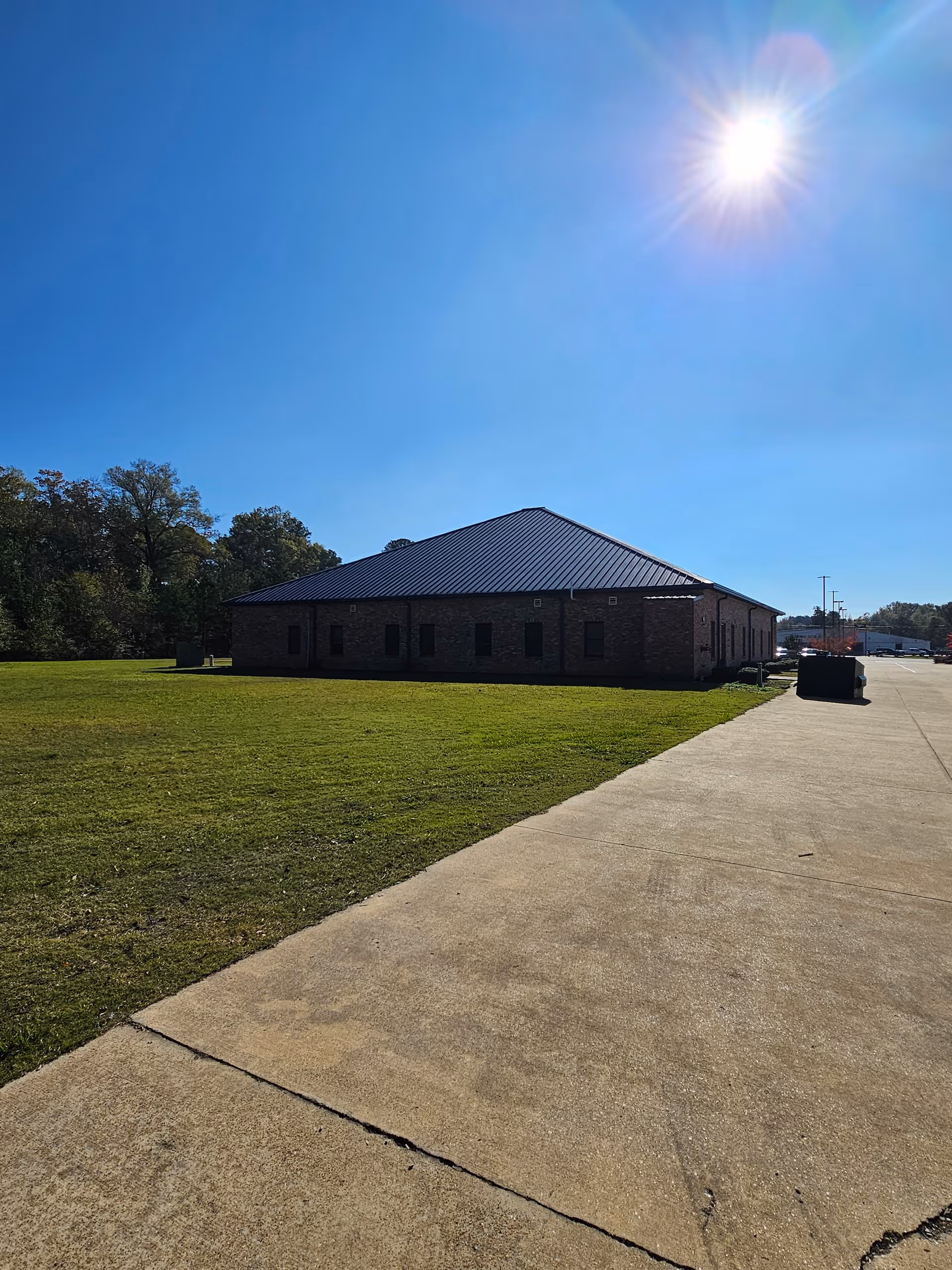 Single brick building with a metal roof on a sunny day beside a grassy lawn.