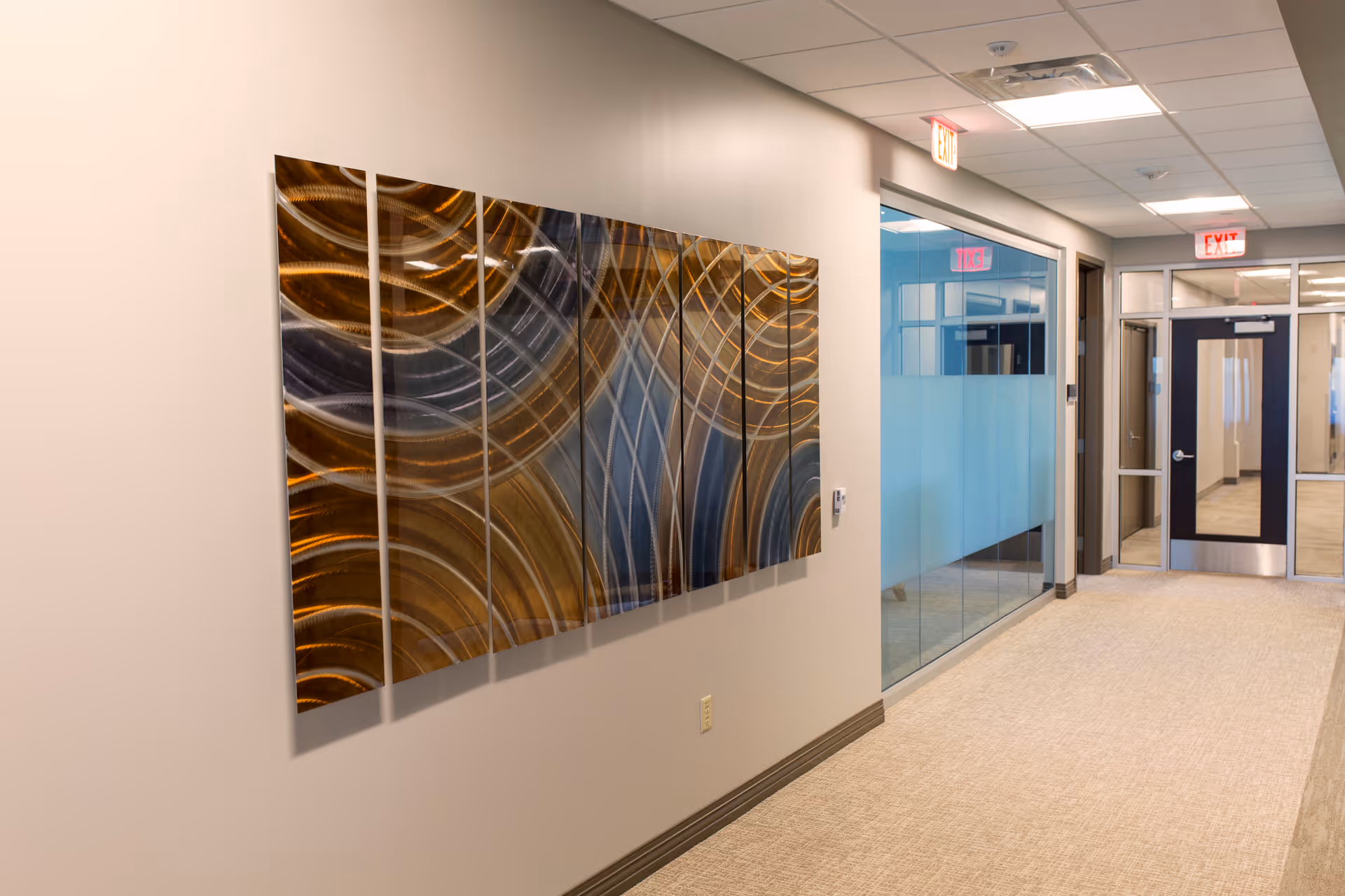 Interior hallway of a senior living facility with wall art, glass partitions, and exit doors.