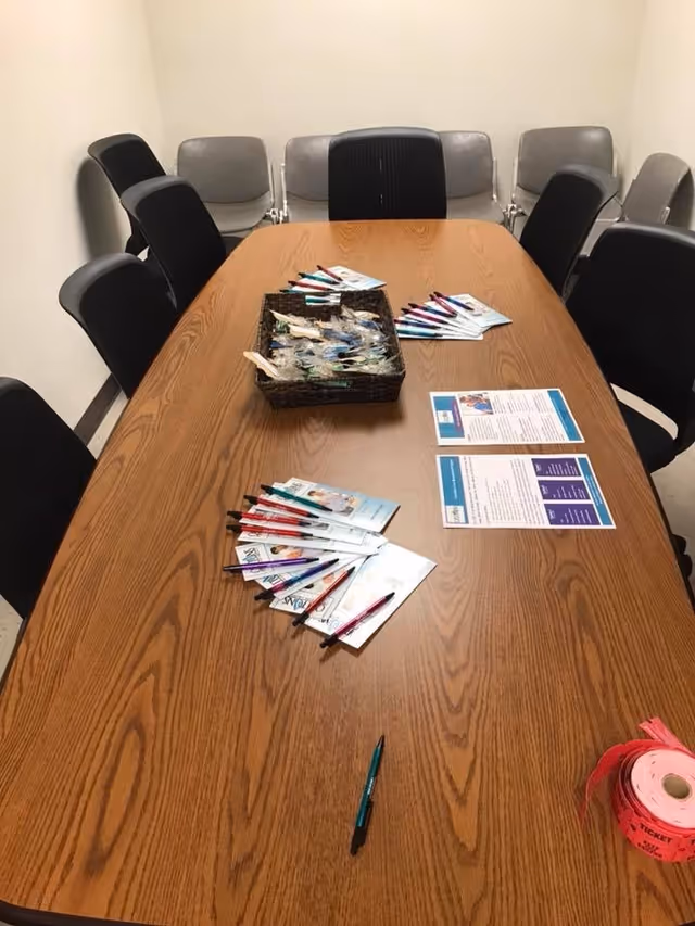 Long wooden conference table with chairs around, pamphlets and a basket in an empty meeting room.