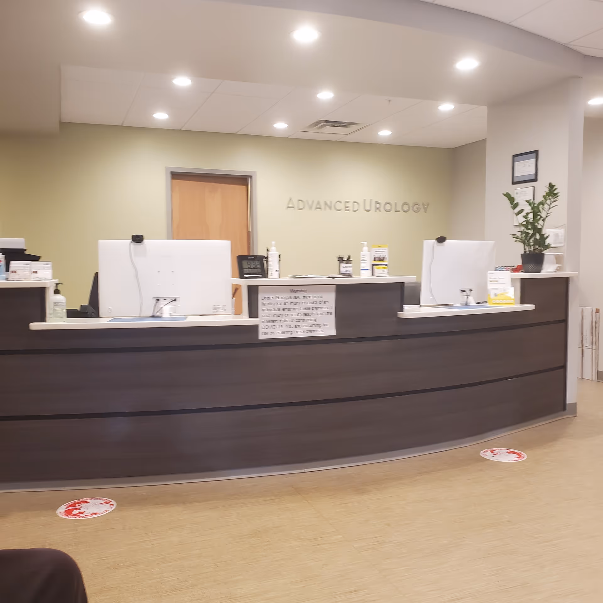Reception desk in a clinic with two computers, a plant, and 'Advanced Urology' sign.