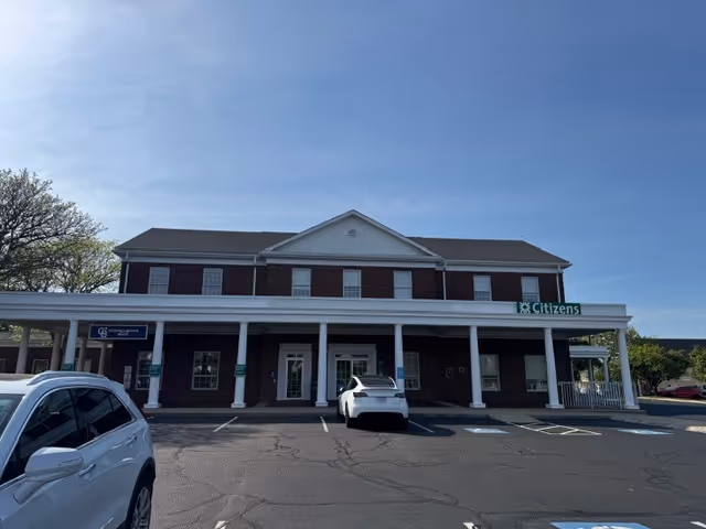 Two-story brick building with white columns and parked cars in front.