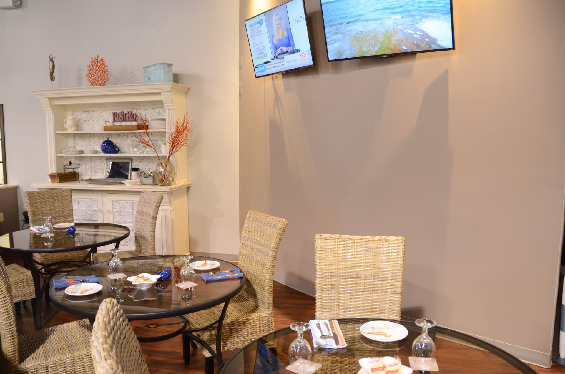 Indoor dining area with round glass tables, wicker chairs, and a wall-mounted TV.