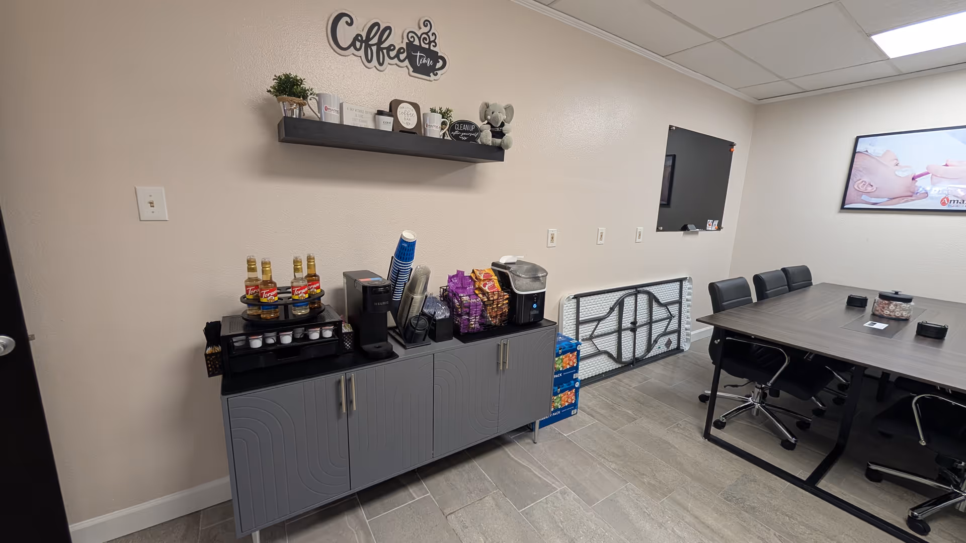 Coffee station with drinks and snacks, cups, and a coffee maker beside a conference table.