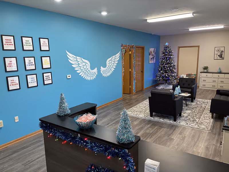 Reception area with blue wall, angel wings mural, Christmas trees, and seating in a senior home.