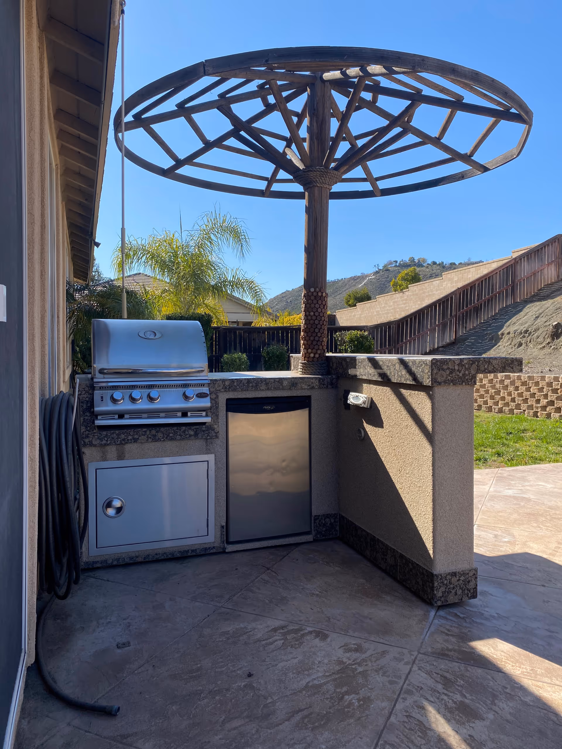 Outdoor patio featuring a built-in grill, stainless cabinets, and a large circular shade structure.