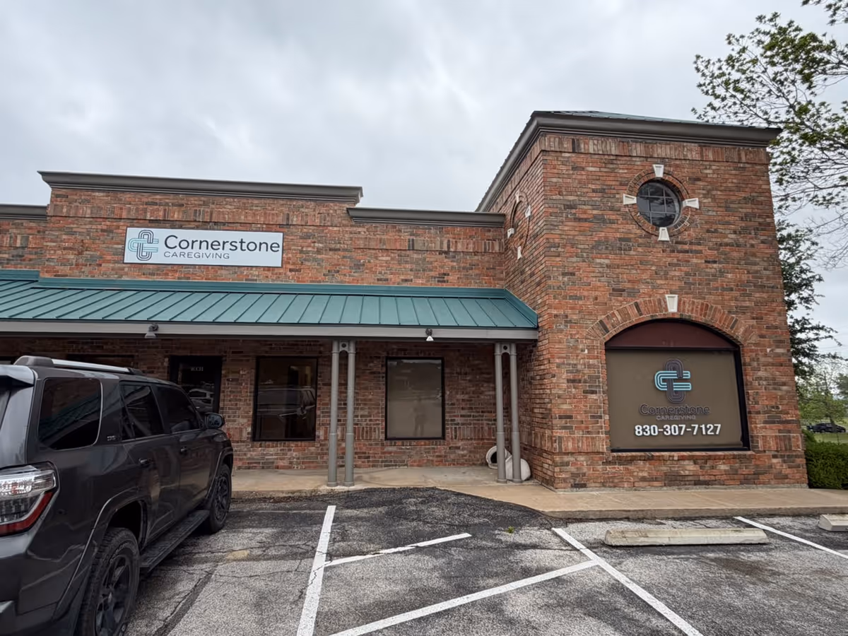 Brick Cornerstone Caregiving building with sign, windows, and a parked SUV in front.