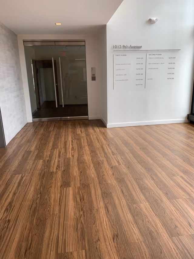 Empty hallway with glass doors and a wall directory in a modern senior living lobby.