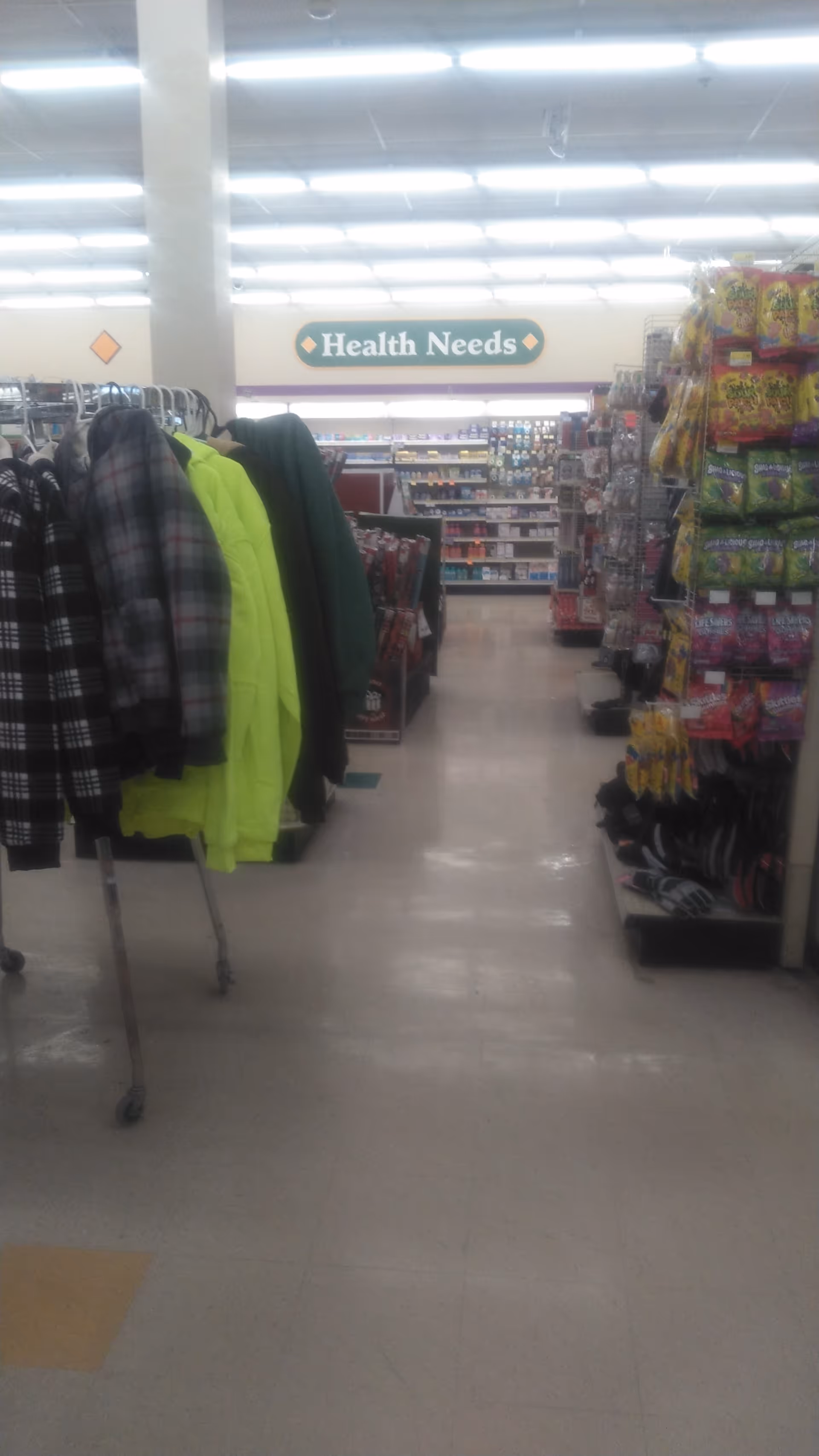 Aisle inside a drugstore with clothing racks and colorful product shelves.