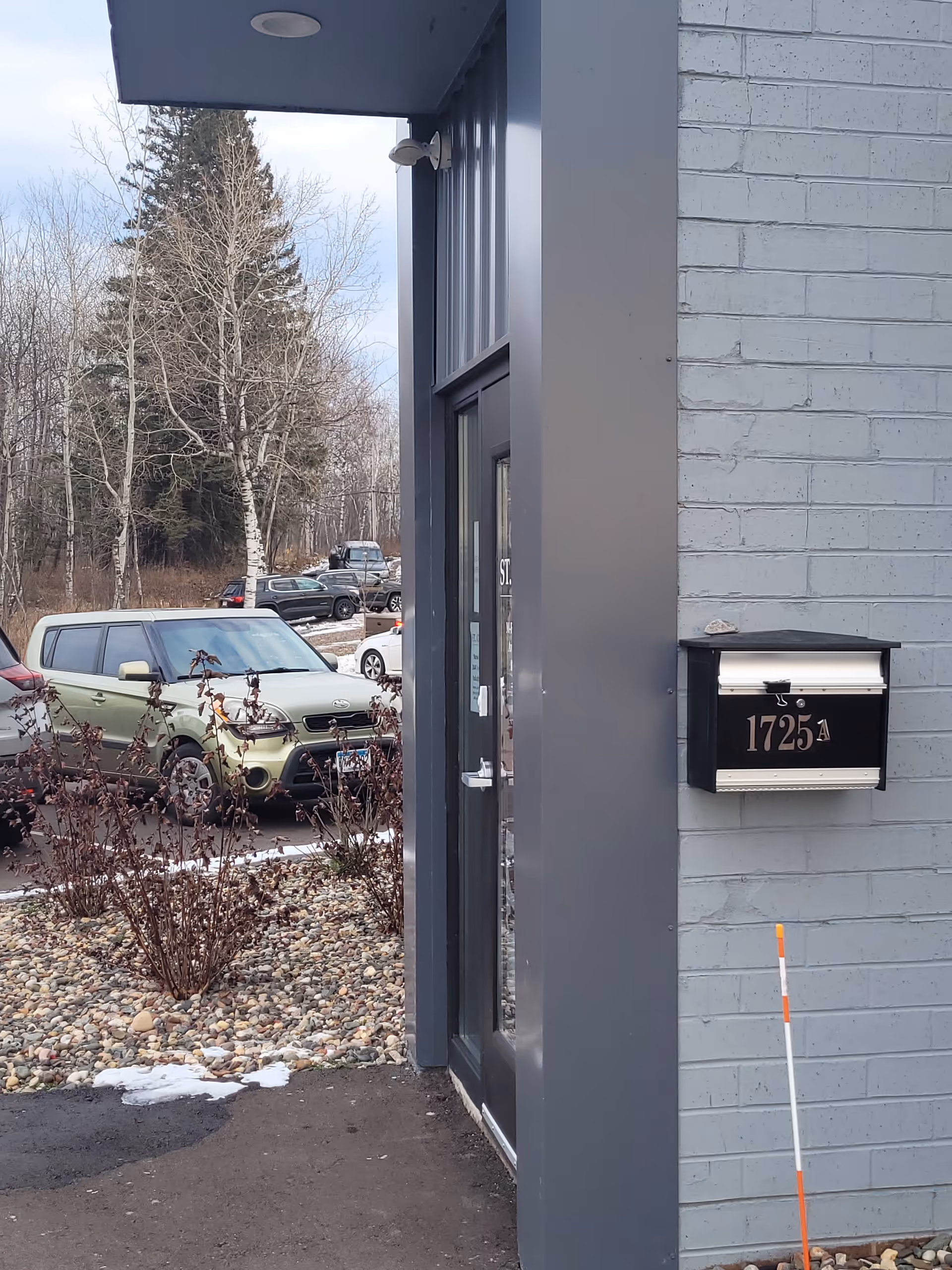 Exterior view of a building entrance with a glass door, mailbox, and parked cars.