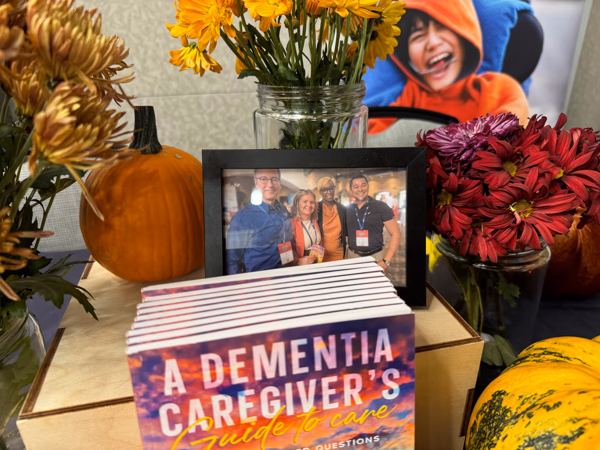 Framed group photo rests among autumn flowers, pumpkins, and a dementia caregiver's guidebook.