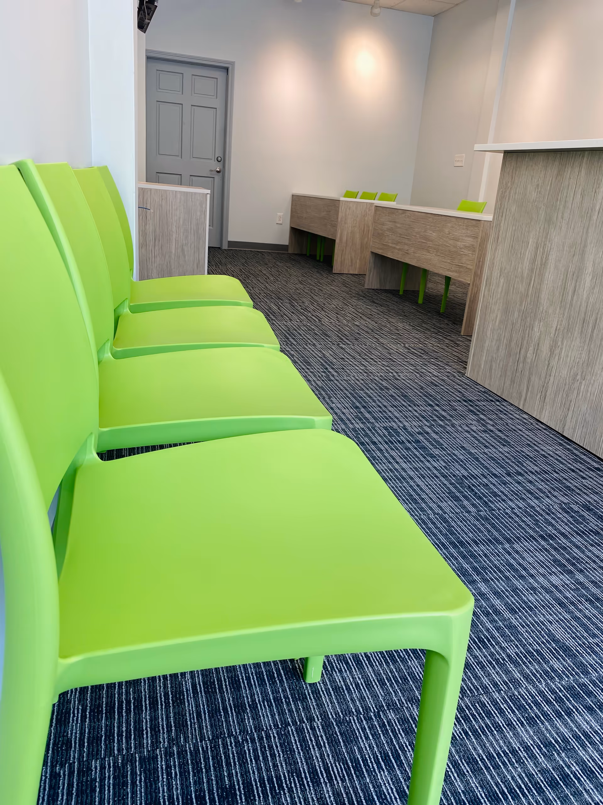 Bright interior lobby with lime green chairs and light wood desks along the wall.