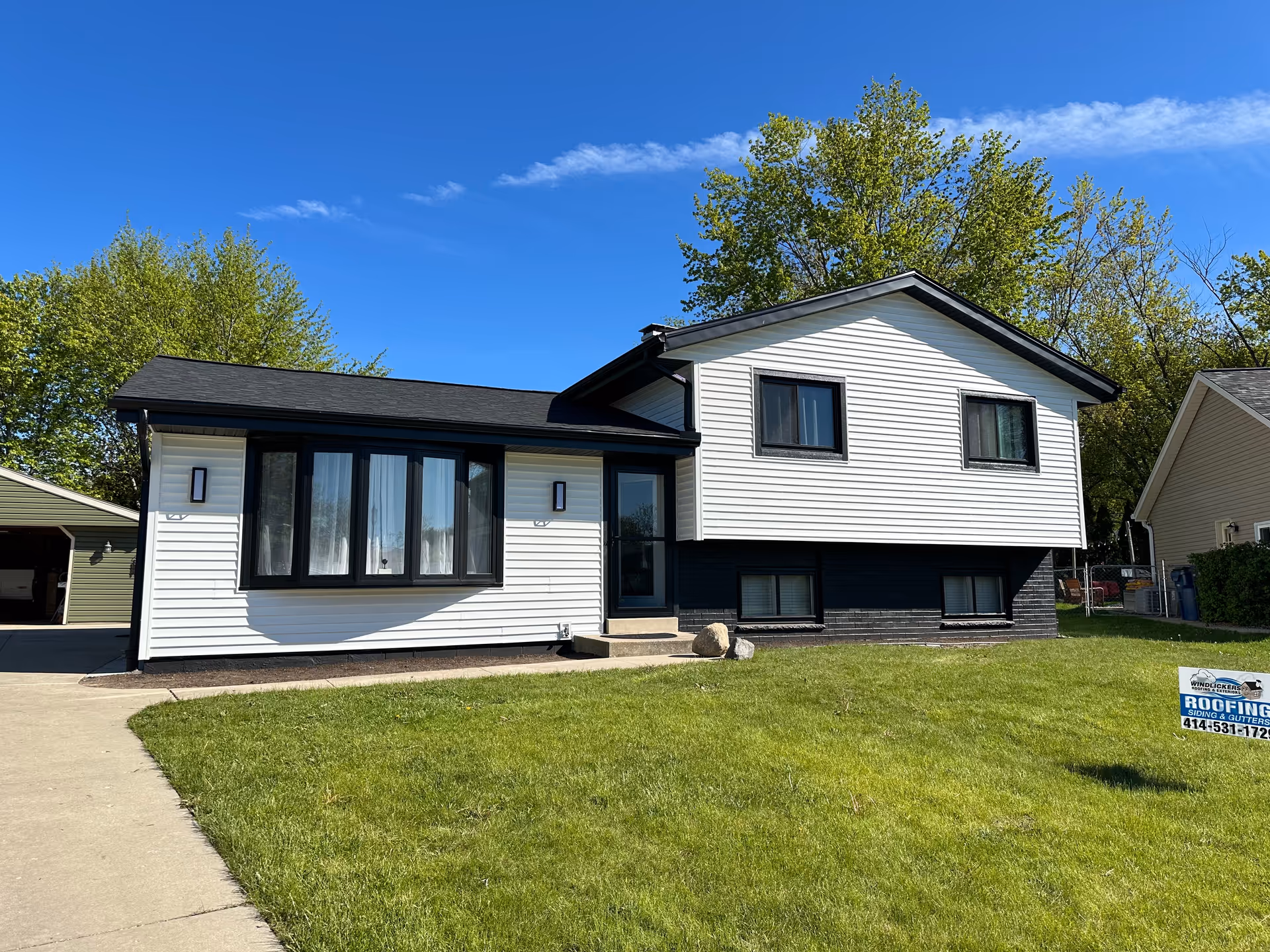 Front view of a two-tone modern house with white siding, black trim, and lawn.