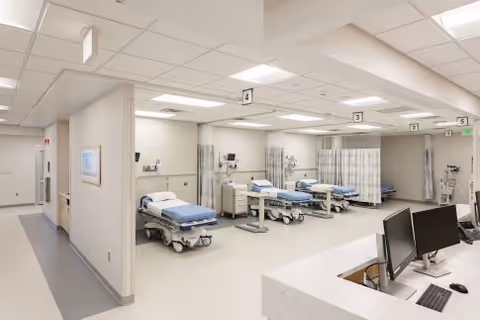 Interior of a long hospital ward with several beds, curtains, and a reception desk.