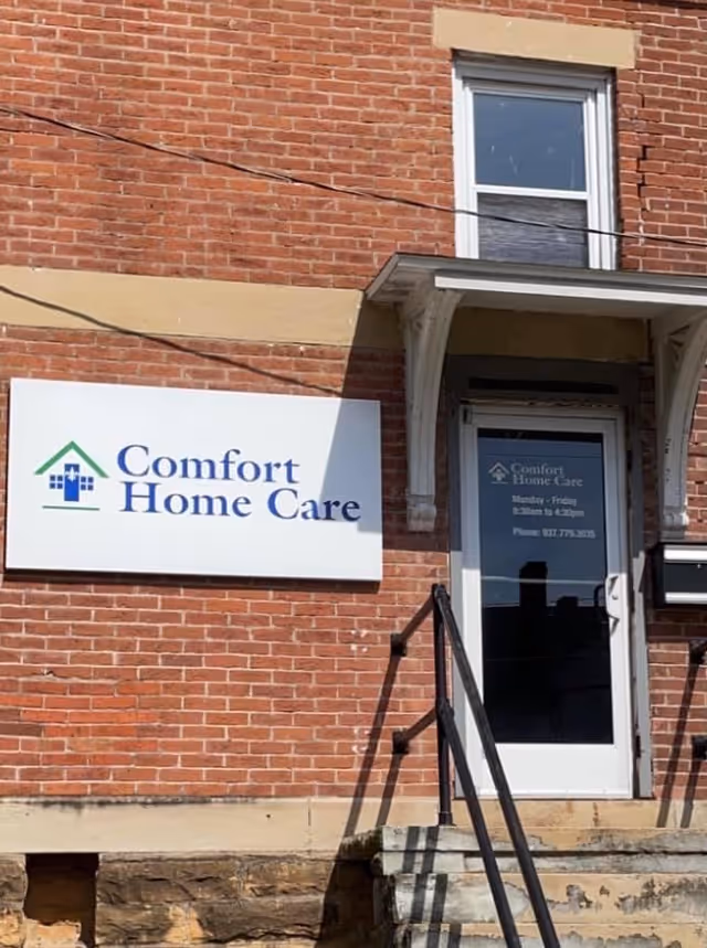 Brick building exterior with a Comfort Home Care sign and entry stairs