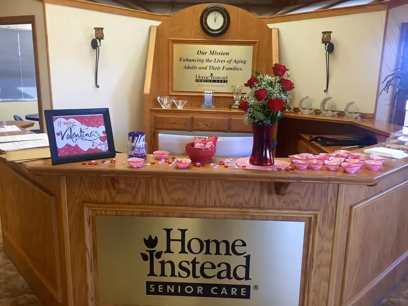 A wooden reception desk with Home Instead signage and Valentine's decorations inside a senior care lobby.