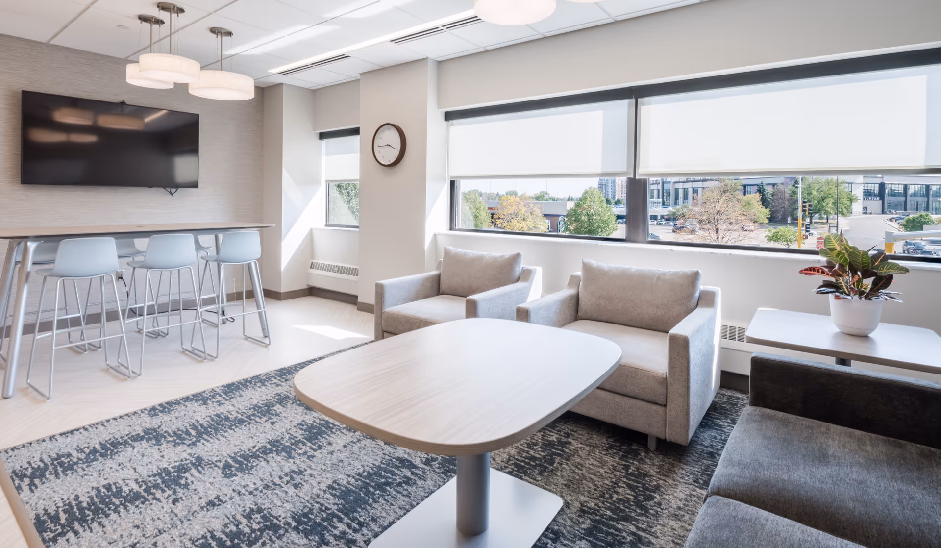 Bright modern lounge area with beige sofas, a coffee table, and a rug by large windows.
