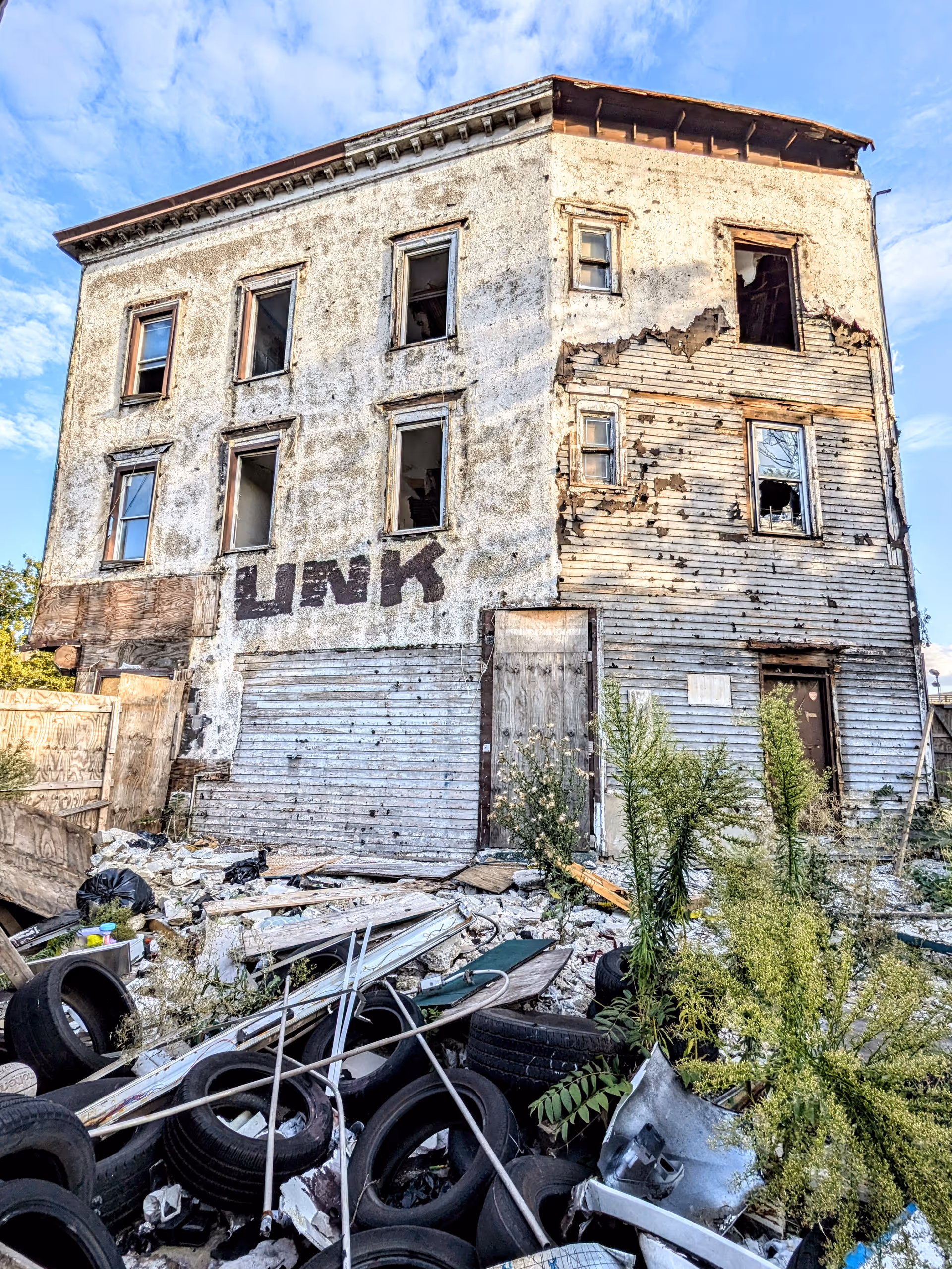 Dilapidated four-story building with peeling siding and rubble-filled foreground.