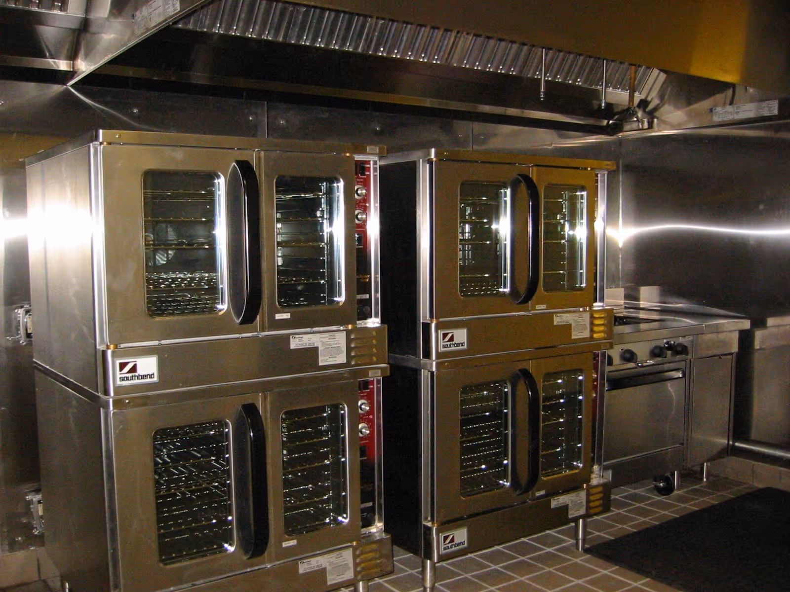 Industrial stainless steel ovens and racks in a commercial kitchen.