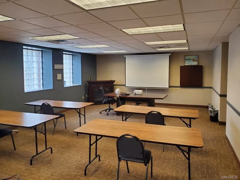 Empty training room with tables, chairs, projector screen, and podium.