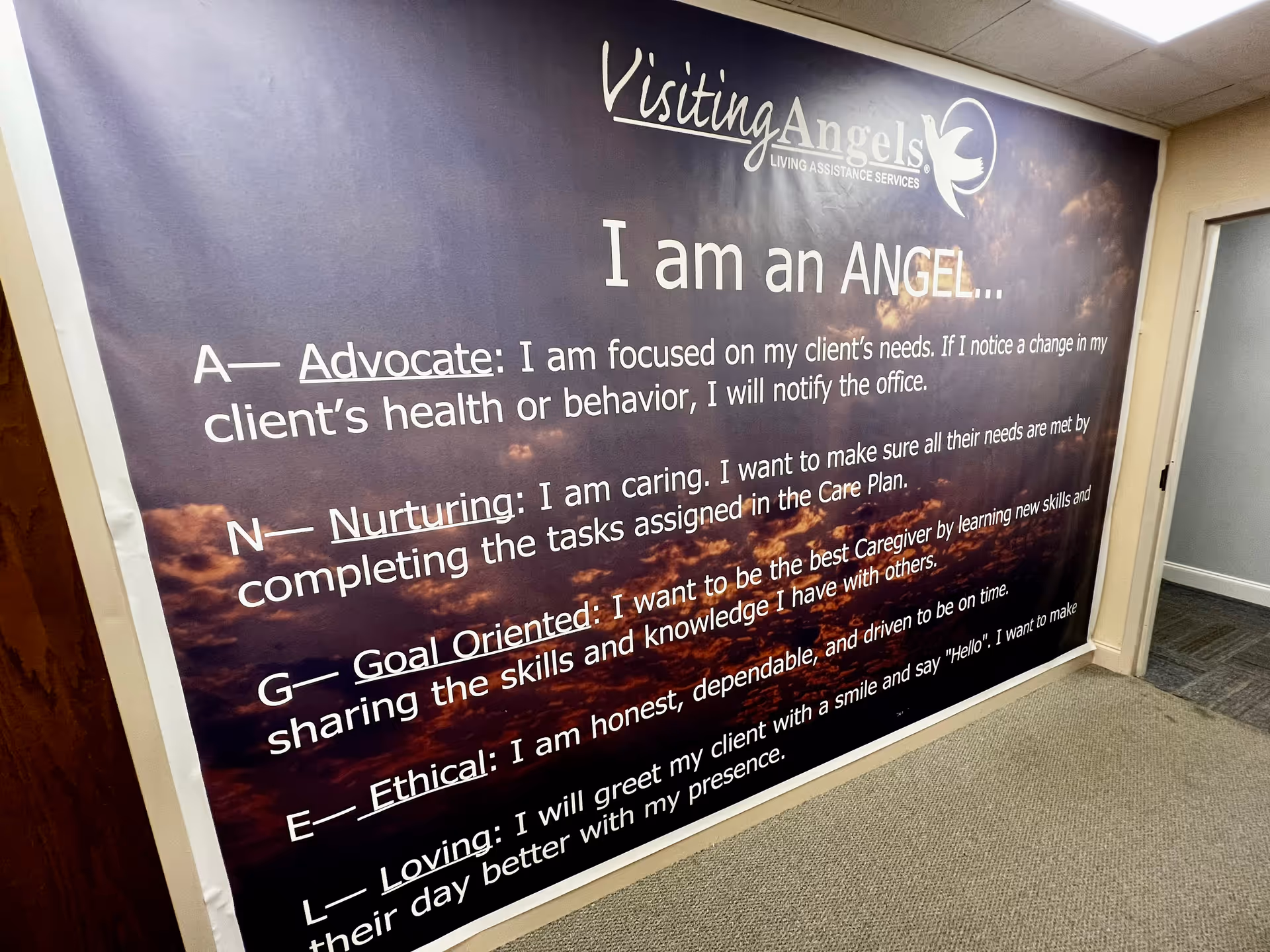 Large wall banner in hallway displays Visiting Angels logo and motivational text.
