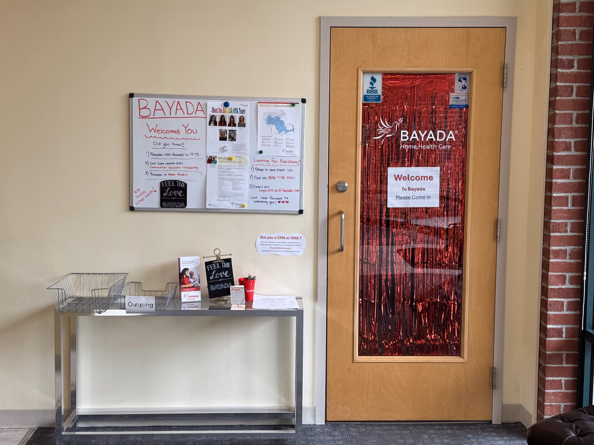 Interior hallway with bulletin board, small table, and a BAYADA door with red fringe.