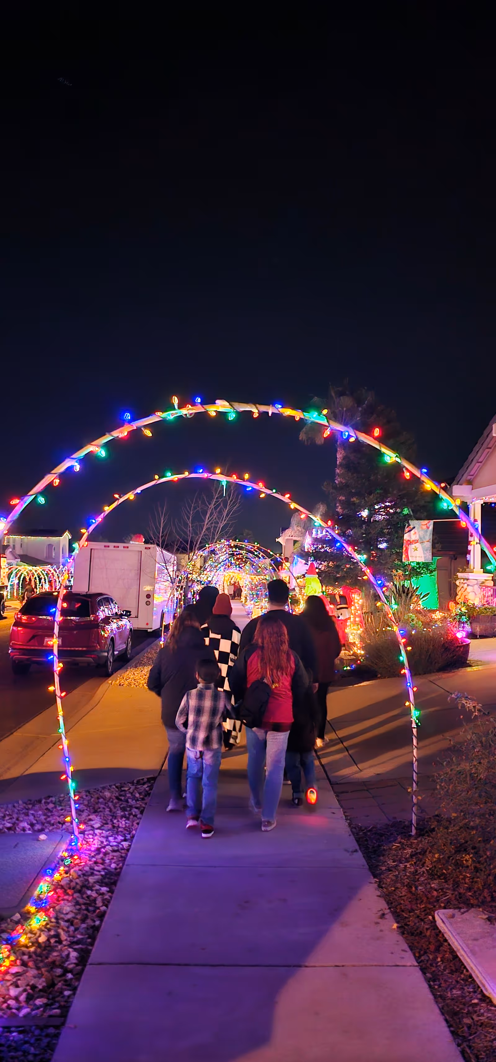 Nighttime outdoor walkway decorated with colorful light arches and people walking.