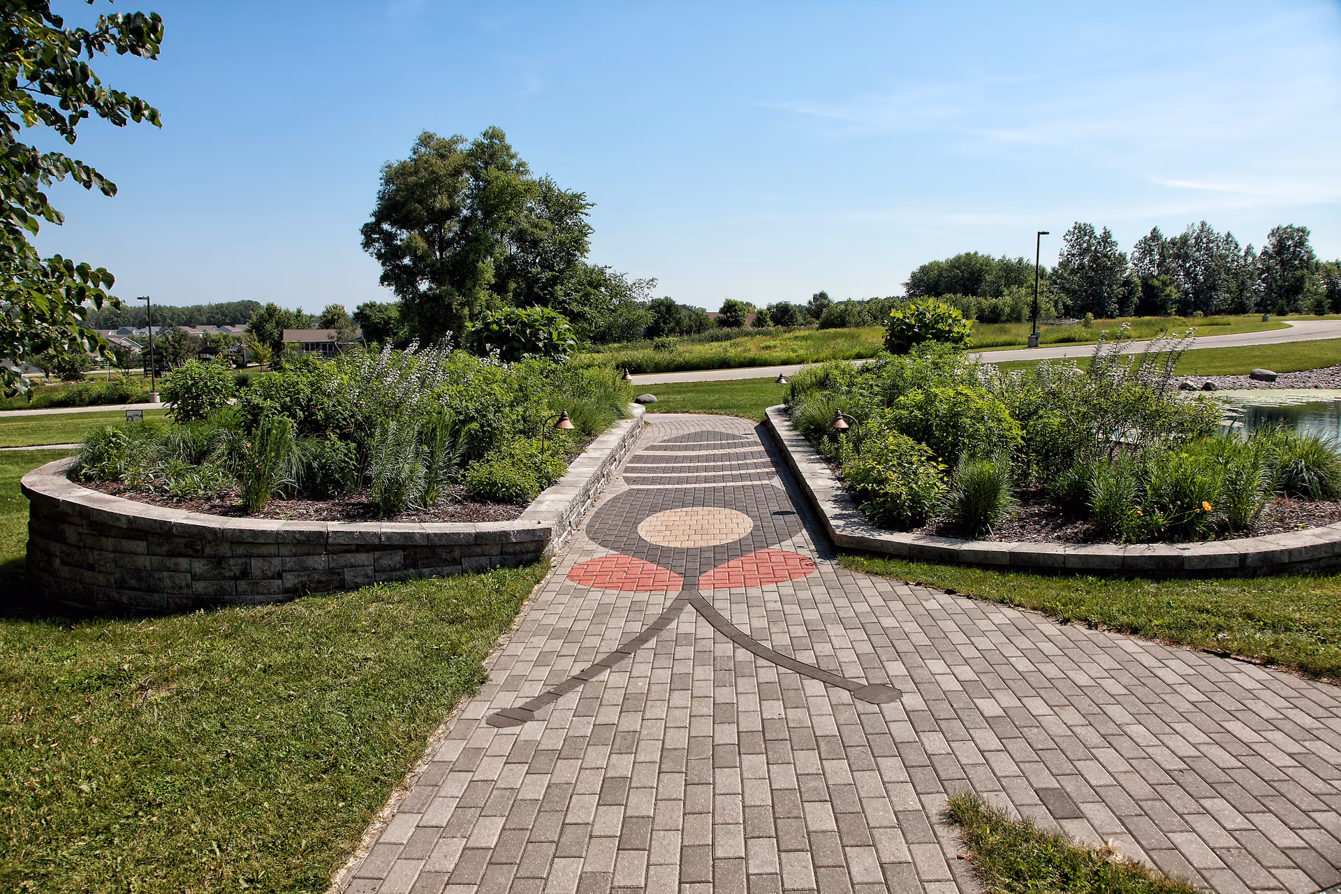 Brick walkway with flower beds and a central decorative pattern in a garden.
