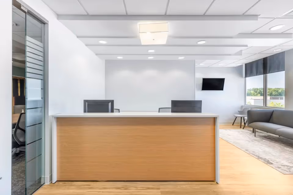 Reception desk in a bright, modern lobby with seating and large windows.