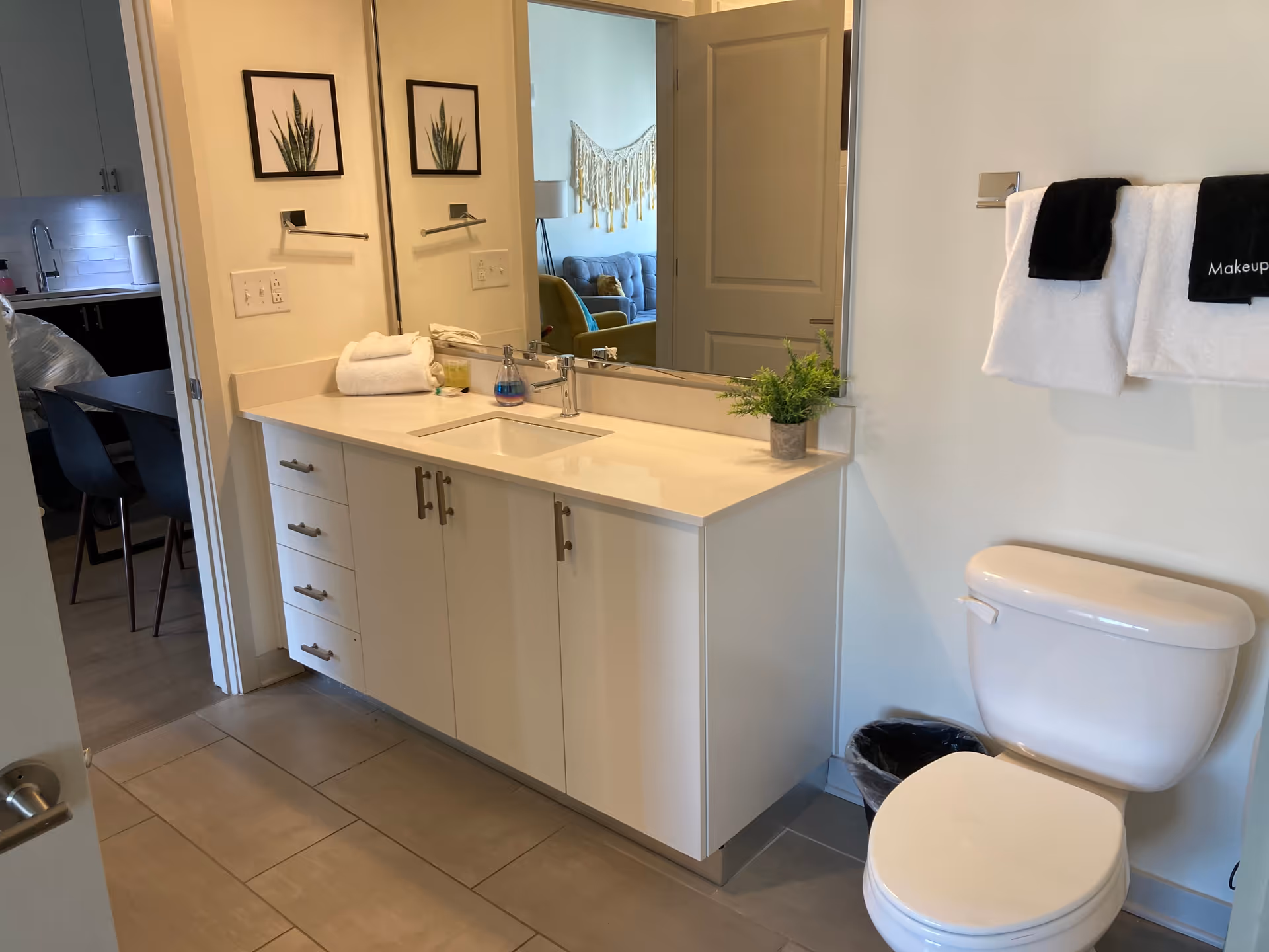 Bright bathroom with white vanity, sink, mirror, towels, and toilet in a residential unit.