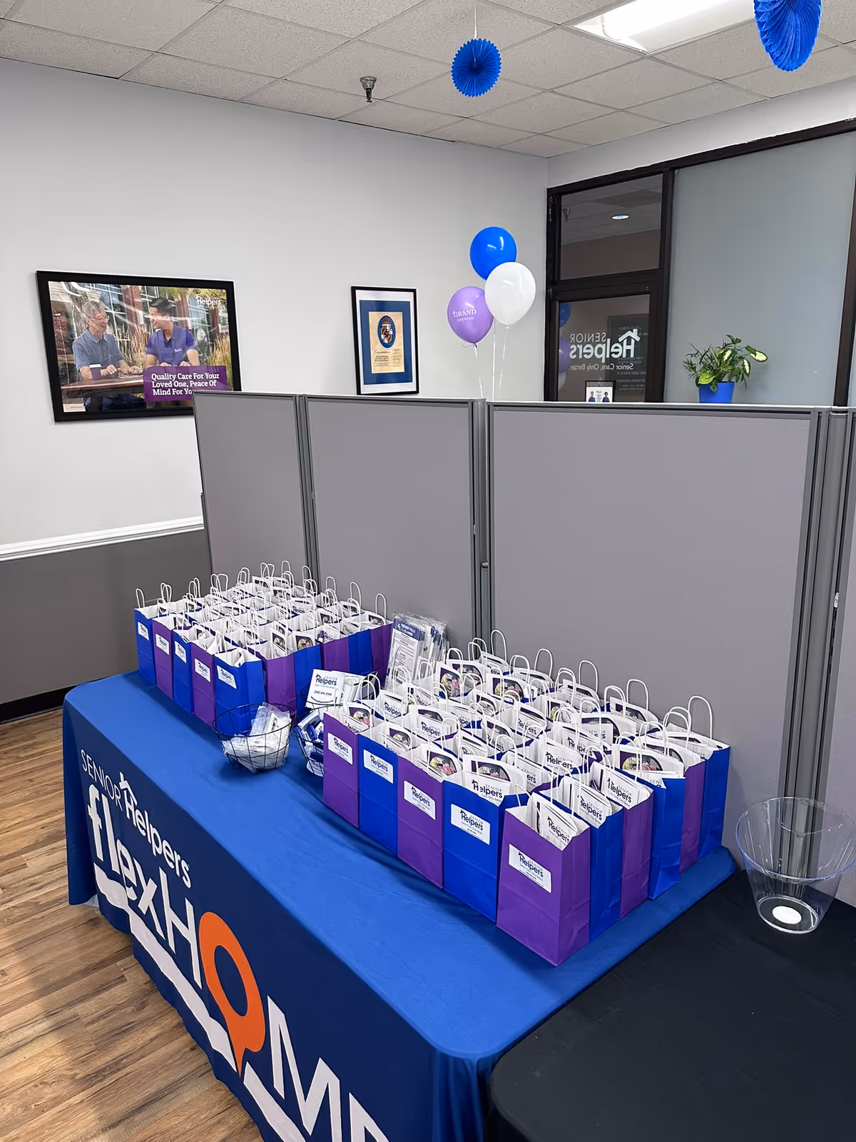 Indoor reception area with many purple and blue gift bags on a blue table.