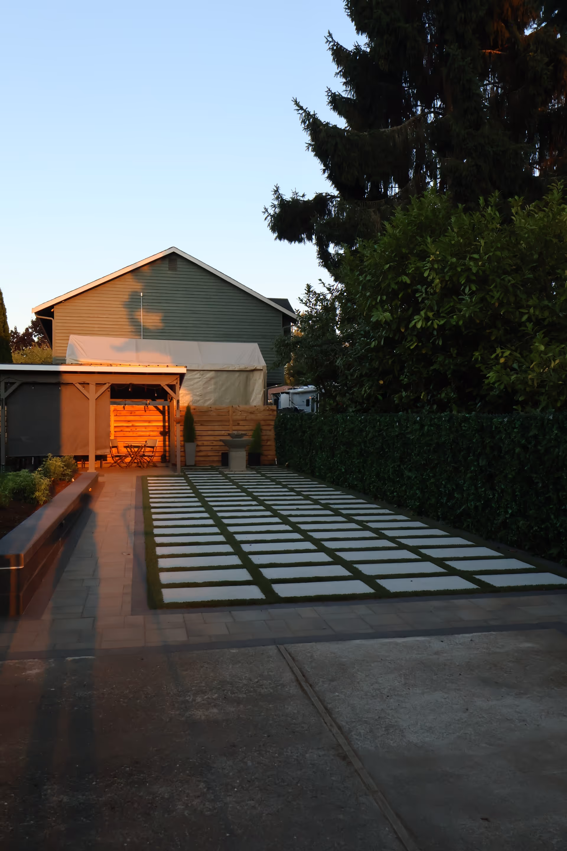 Outdoor courtyard with stepping stone path, hedge, and patio seating near a building.