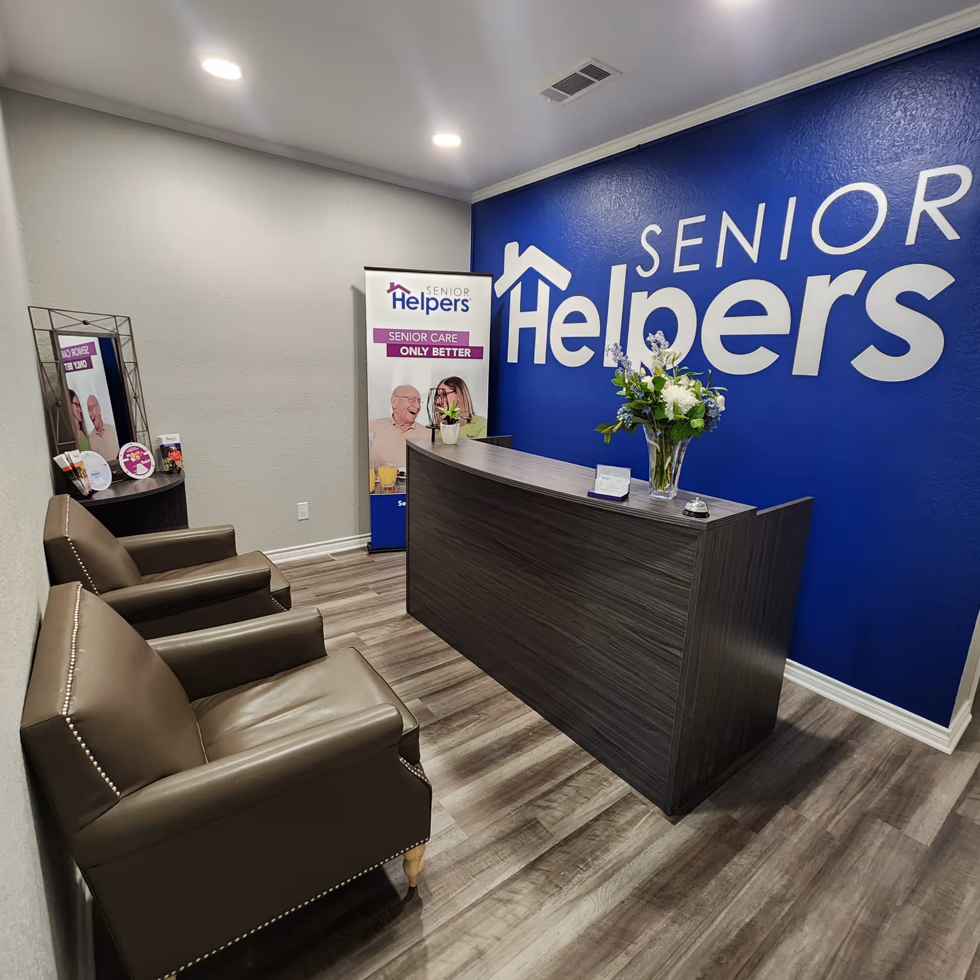 Reception area featuring a dark desk, blue wall with Senior Helpers signage, and seating.