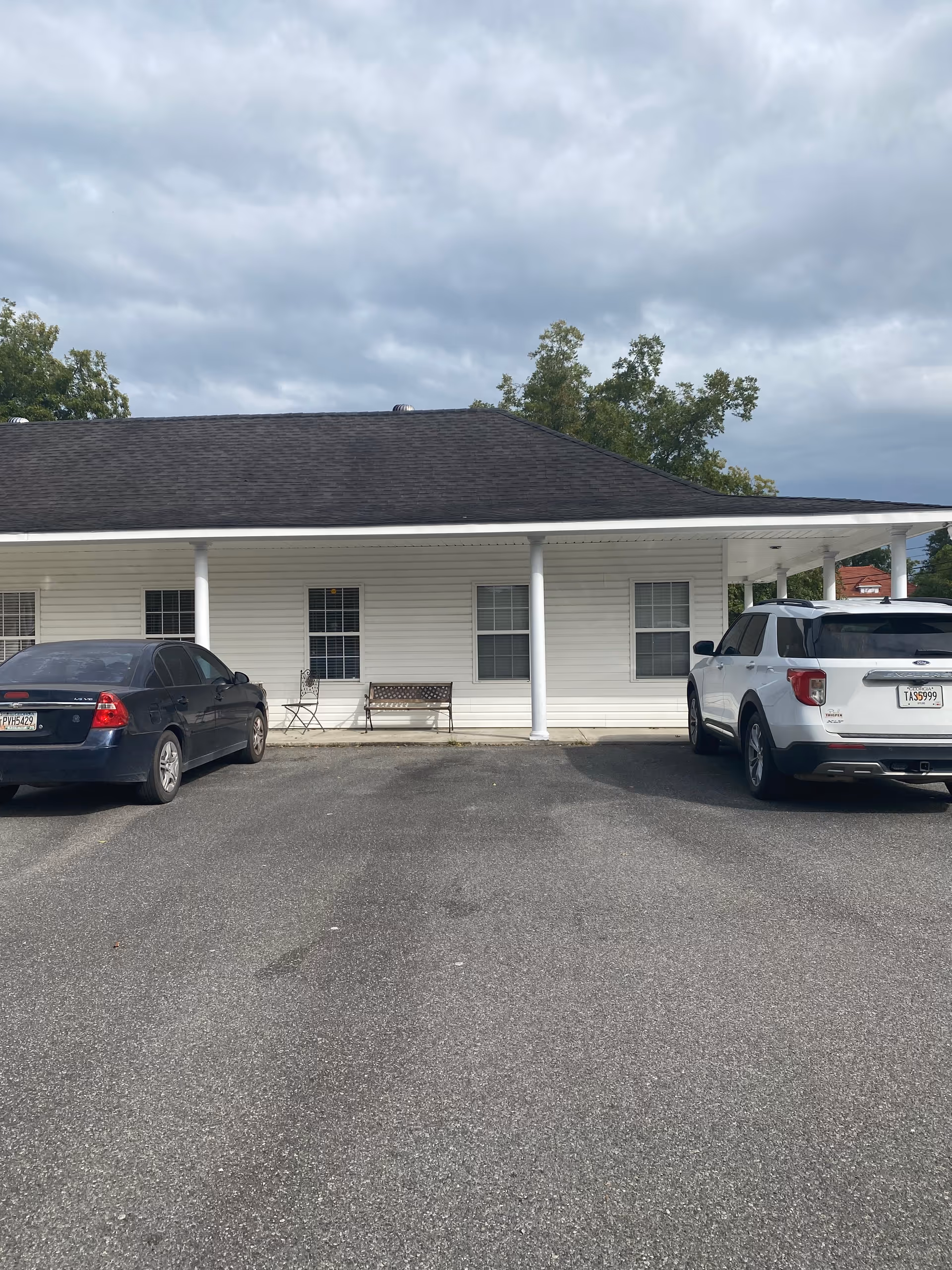 White, single-story building with a covered front porch and parked cars in front.