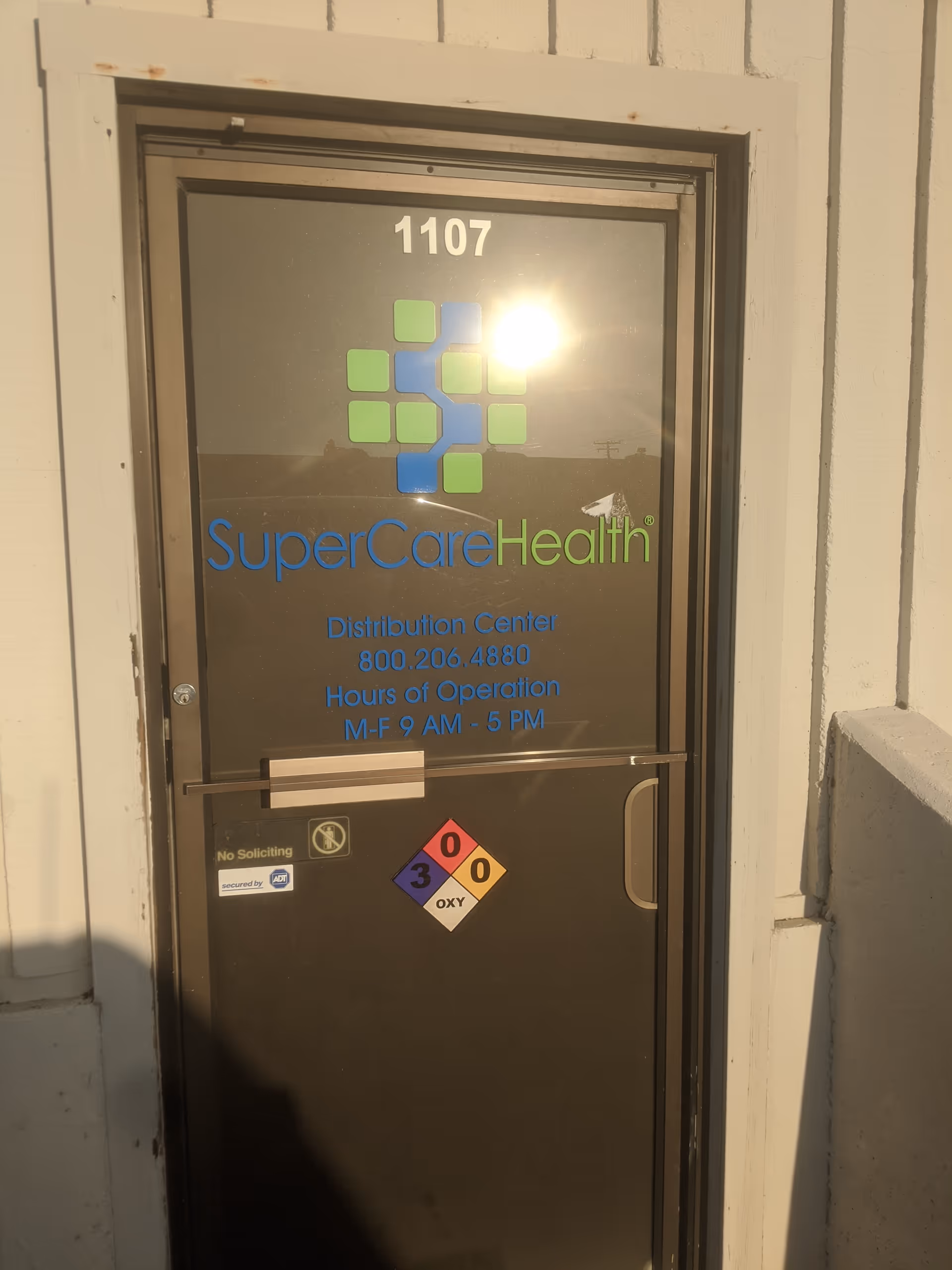Exterior door of SuperCare Health building displaying logo, address 1107, and hours.
