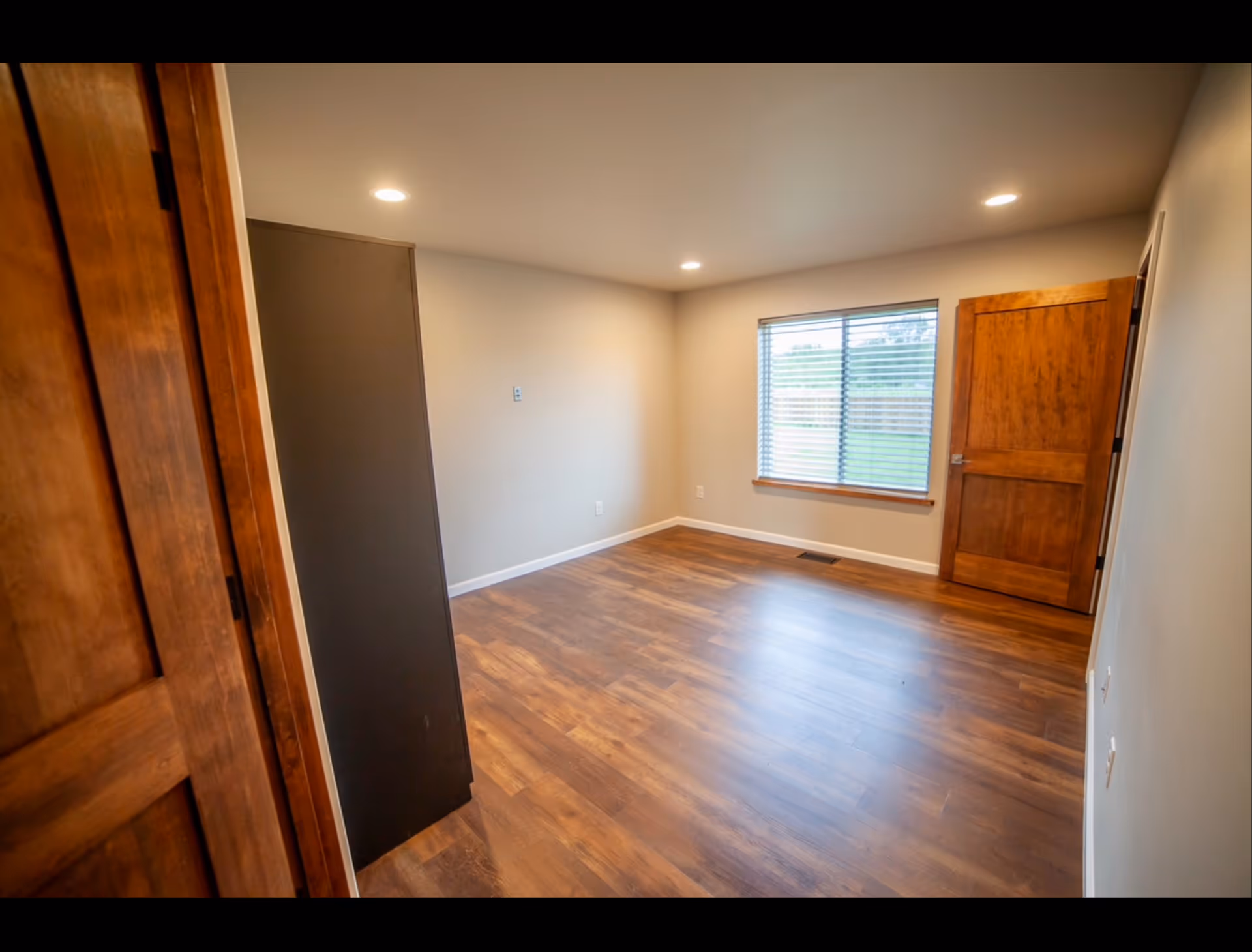 Empty interior room with hardwood floor, window, and wooden doors in a senior living home.