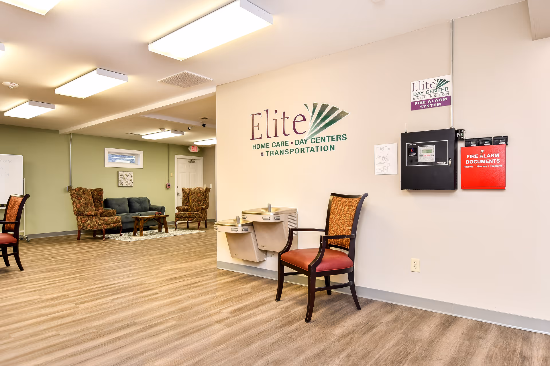 Interior lobby area of Elite Home Care Day Centers with seating and a logo on wall.