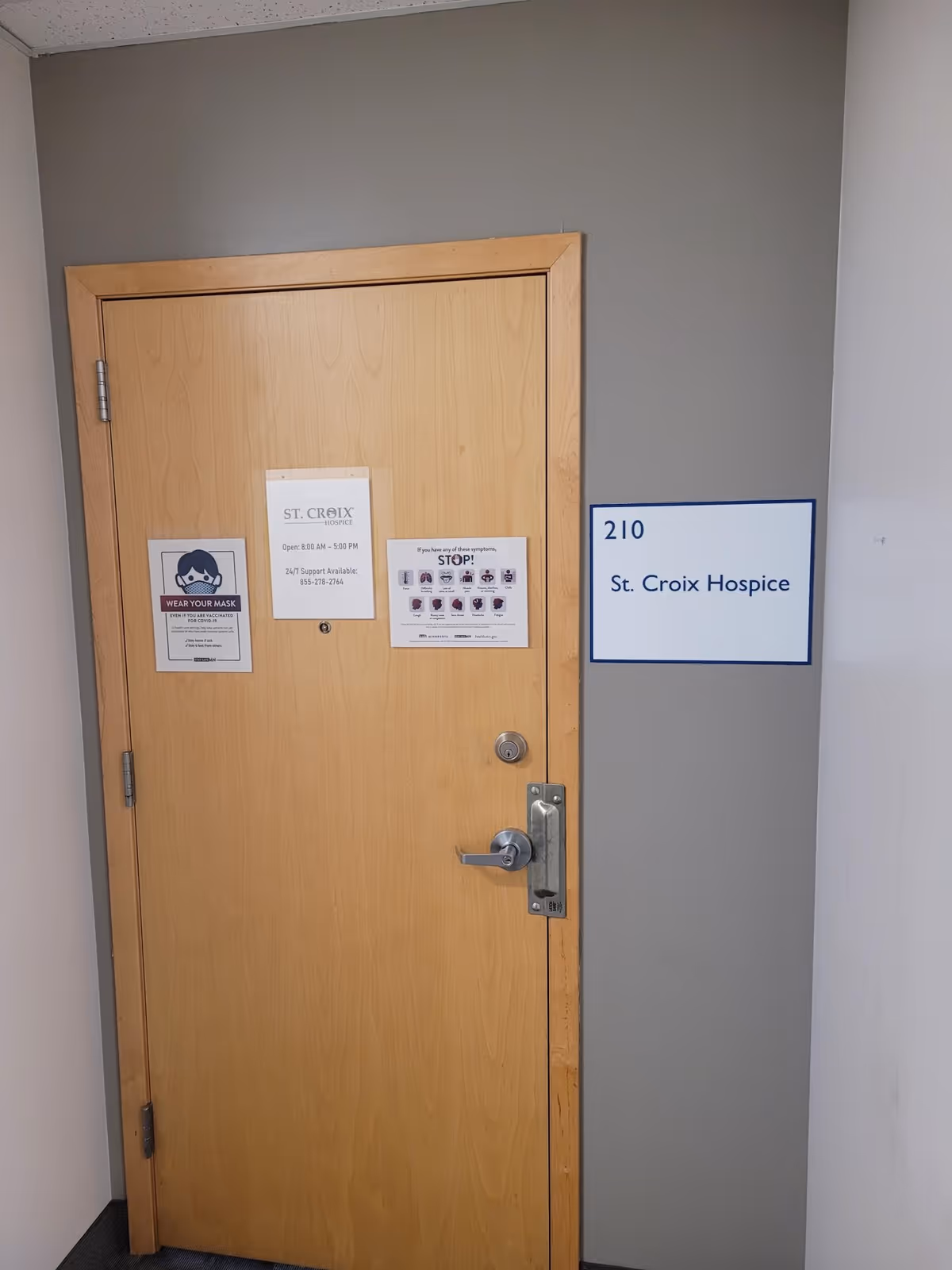 A wooden door in a gray hall with a St. Croix Hospice sign beside it.