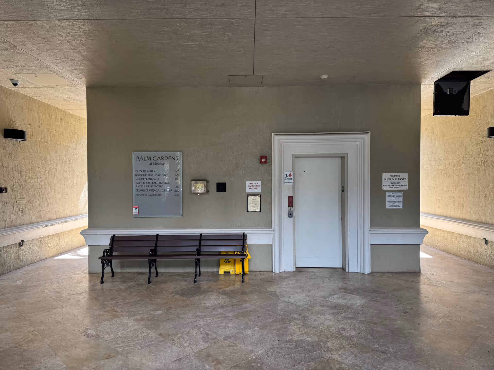 Interior hallway with bench, beige walls, central door, and wall plaques.