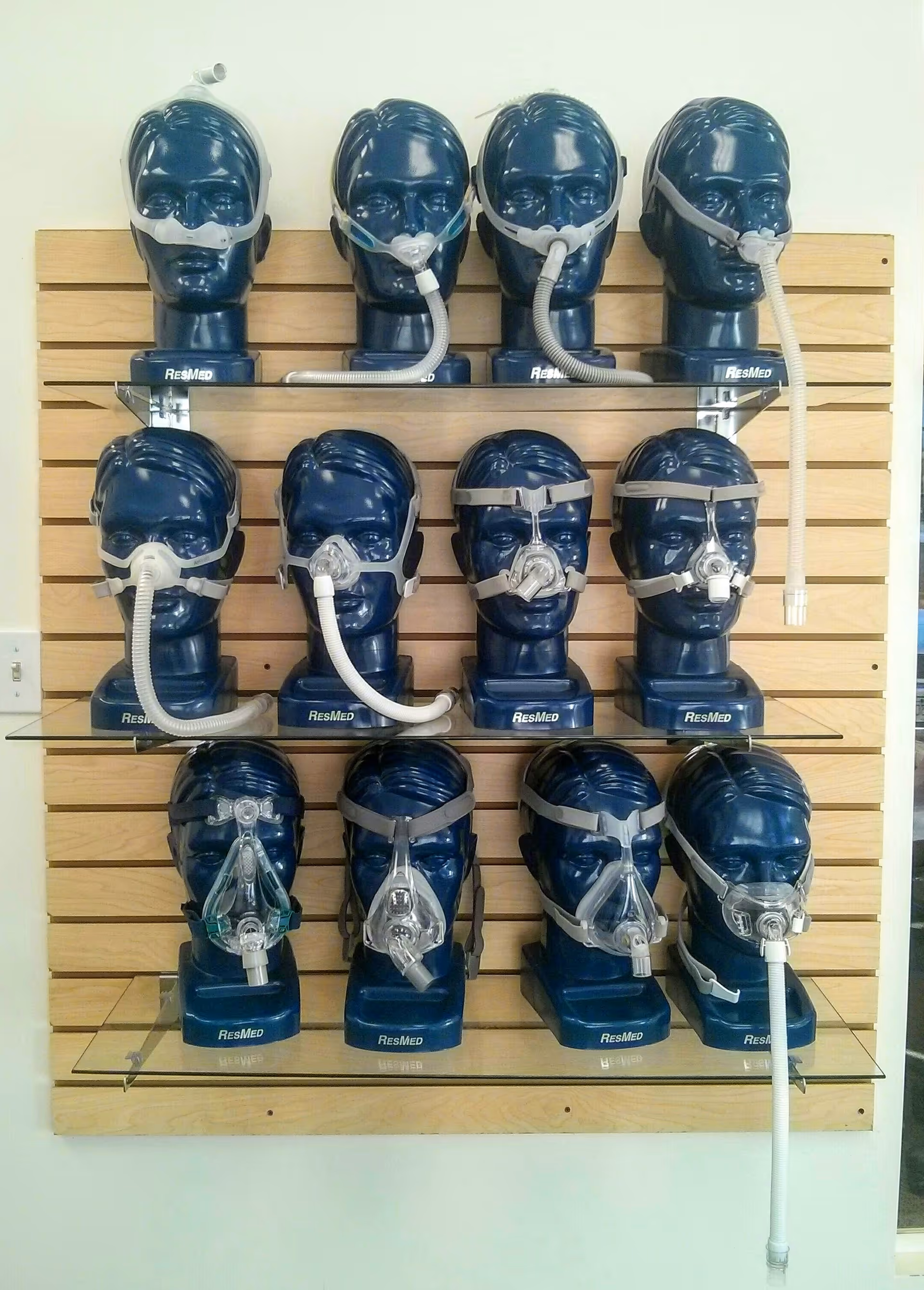 Wall-mounted display of blue CPAP masks on mannequin heads arranged in a grid.