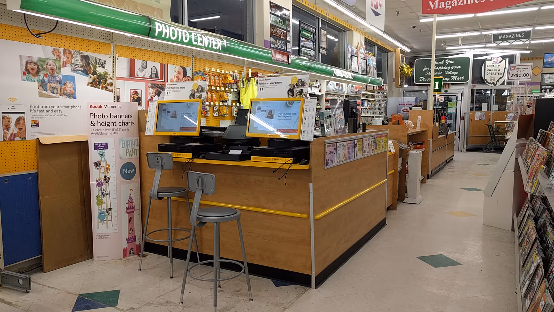 Inside a Discount Drug Mart, checkout counters, magazines and a photo center.