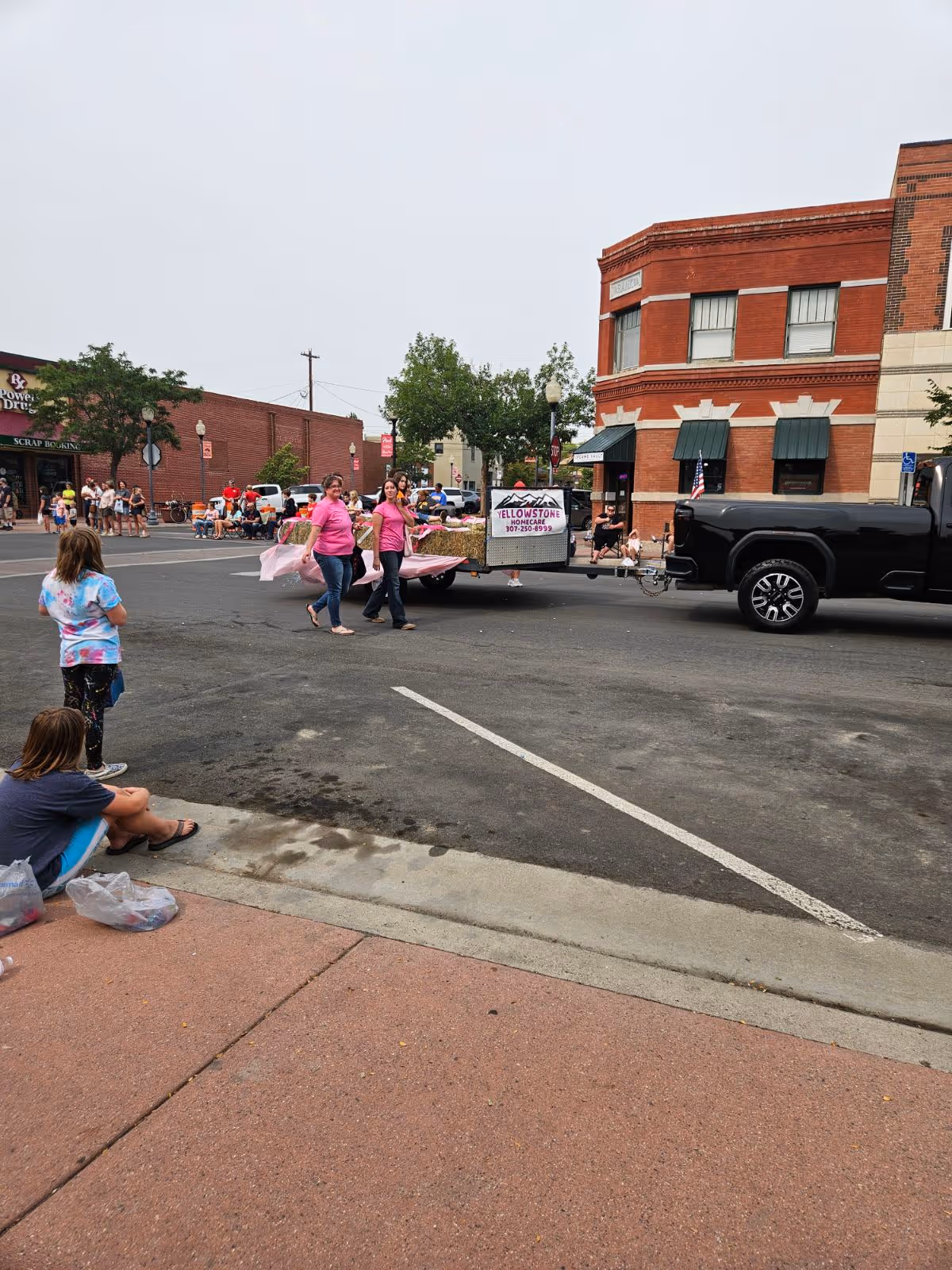 Parade on downtown street with Yellowstone Homecare trailer and cheering spectators.