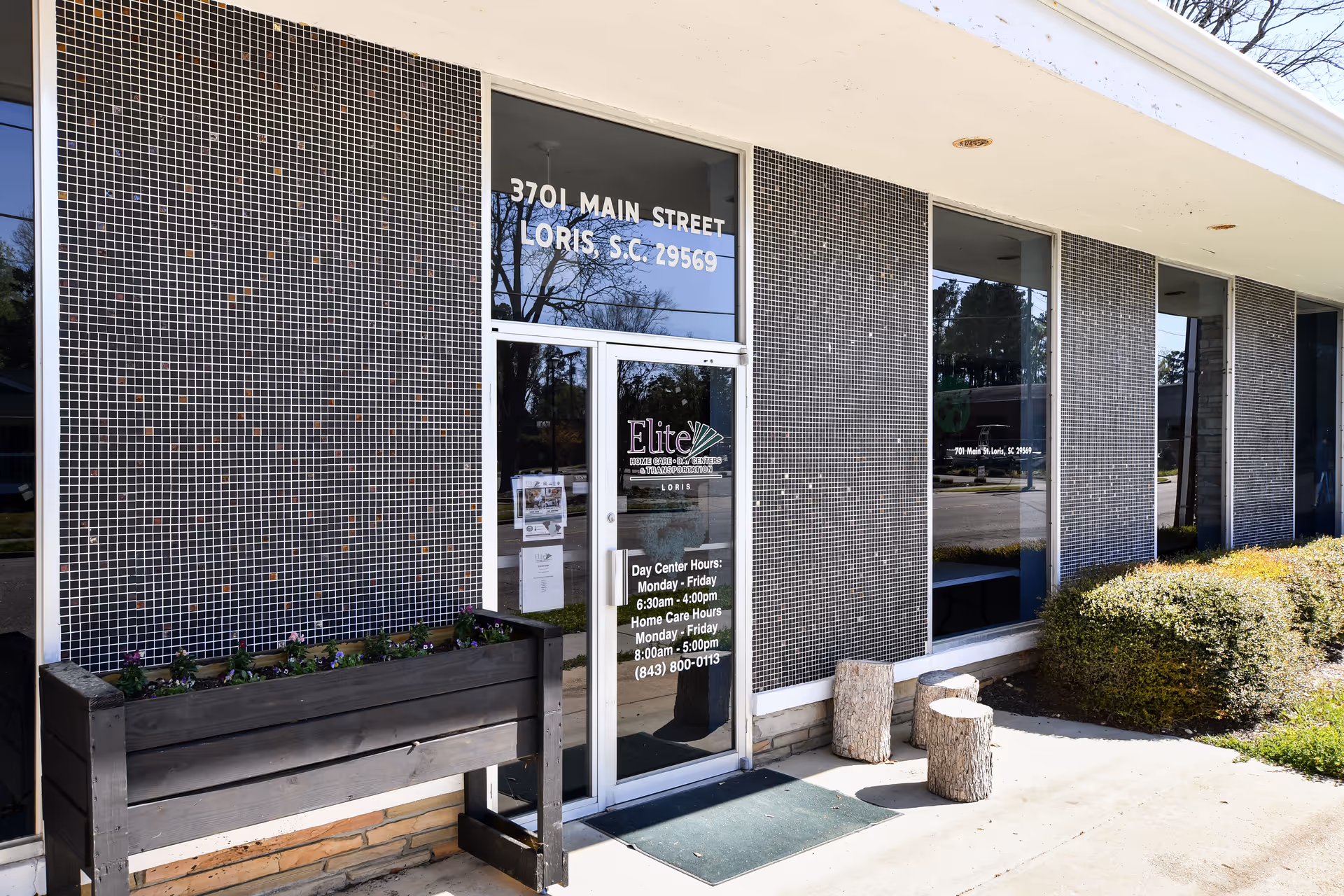 Front exterior of Elite Home Care and Day Centers, with entrance, tiled walls, and planters.